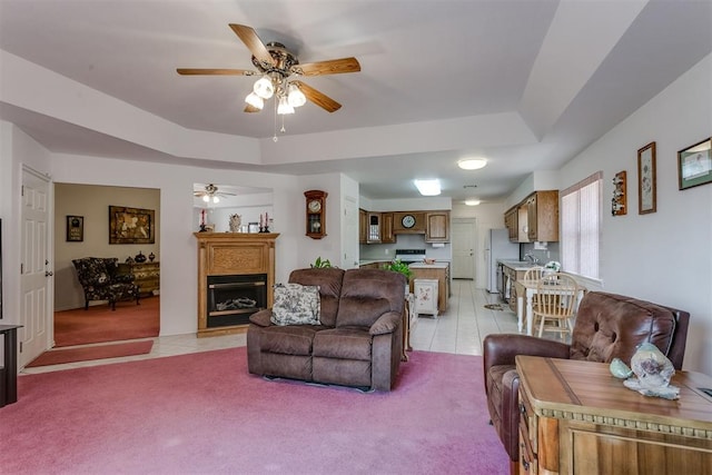 living room with a tray ceiling, ceiling fan, sink, and light colored carpet