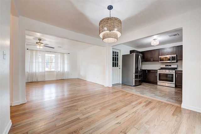 kitchen featuring light wood-type flooring, dark brown cabinetry, stainless steel appliances, ceiling fan with notable chandelier, and pendant lighting