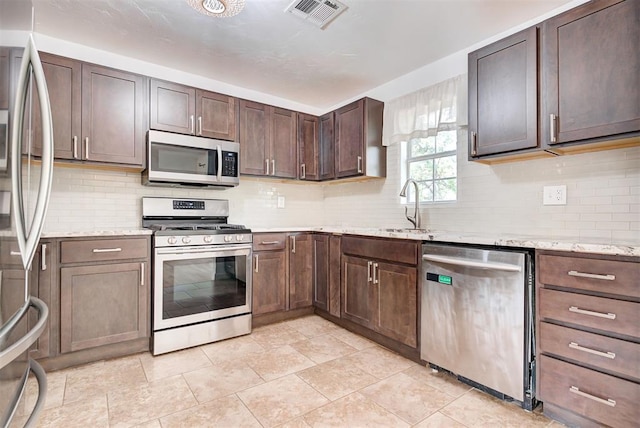 kitchen featuring decorative backsplash, appliances with stainless steel finishes, light stone counters, dark brown cabinetry, and sink