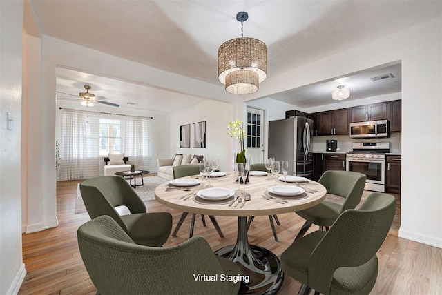 dining room with ceiling fan with notable chandelier and light hardwood / wood-style floors