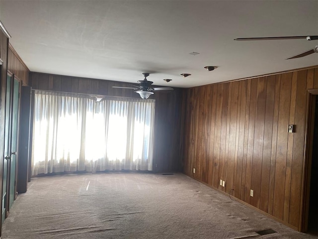 carpeted spare room with ceiling fan and wood walls