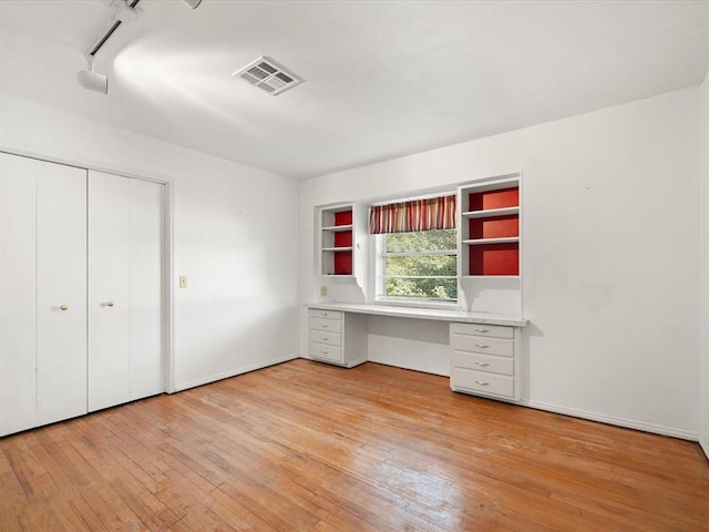 unfurnished office with light hardwood / wood-style floors, built in desk, and rail lighting