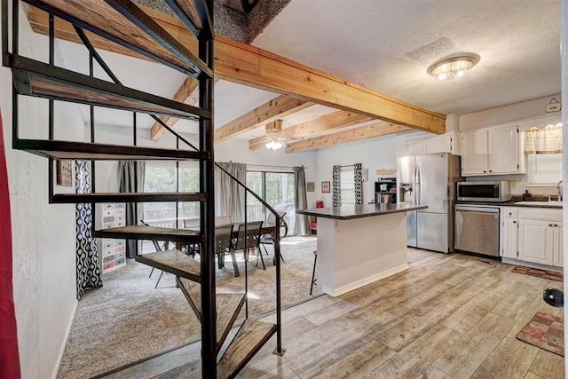 kitchen with beam ceiling, appliances with stainless steel finishes, light hardwood / wood-style floors, a kitchen bar, and white cabinetry