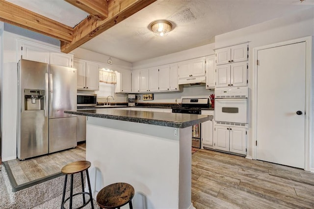 kitchen with beam ceiling, white cabinetry, stainless steel appliances, and light hardwood / wood-style floors