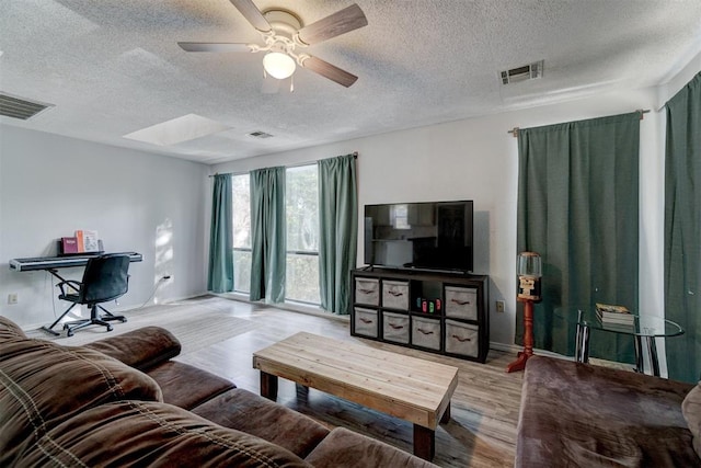 living room featuring a skylight, ceiling fan, light hardwood / wood-style floors, and a textured ceiling