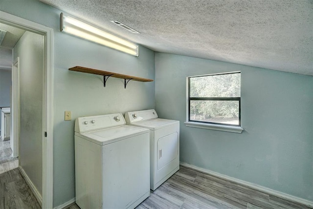 laundry area featuring washing machine and clothes dryer, light hardwood / wood-style floors, and a textured ceiling