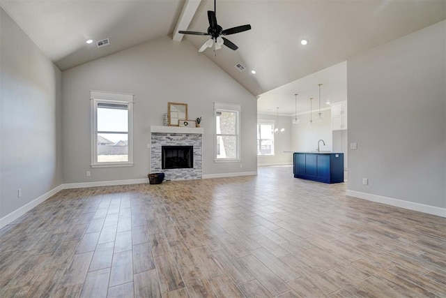 unfurnished living room featuring ceiling fan with notable chandelier, light wood-type flooring, sink, and high vaulted ceiling