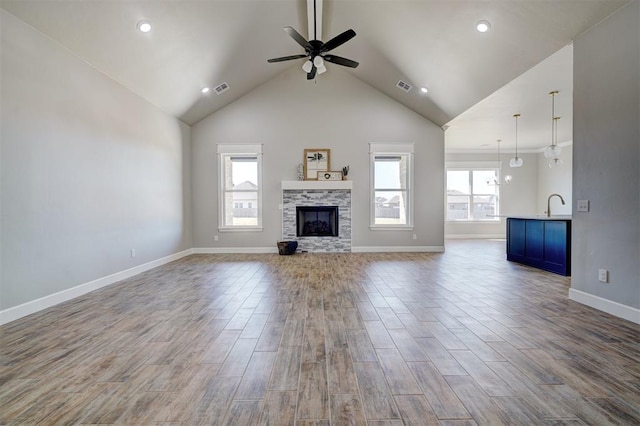 unfurnished living room featuring ceiling fan, sink, high vaulted ceiling, a fireplace, and light wood-type flooring