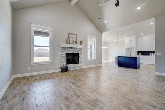 unfurnished living room featuring ceiling fan with notable chandelier, sink, high vaulted ceiling, a fireplace, and light hardwood / wood-style floors