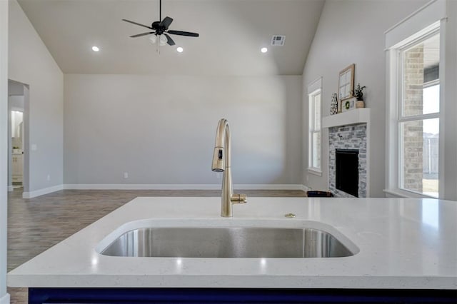 kitchen with light stone countertops, sink, hardwood / wood-style floors, a stone fireplace, and lofted ceiling