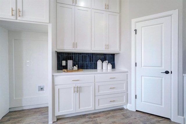 bar with decorative backsplash, light wood-type flooring, and white cabinetry