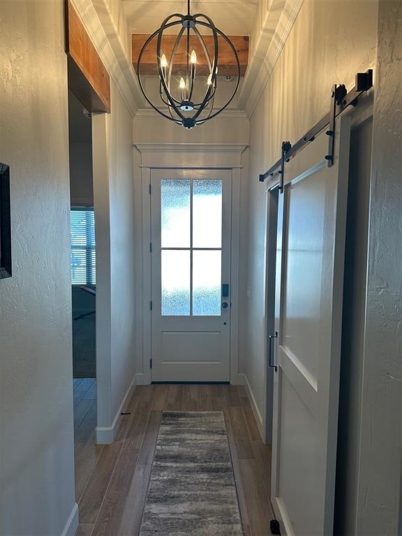 doorway to outside featuring dark hardwood / wood-style floors, a barn door, ornamental molding, and an inviting chandelier