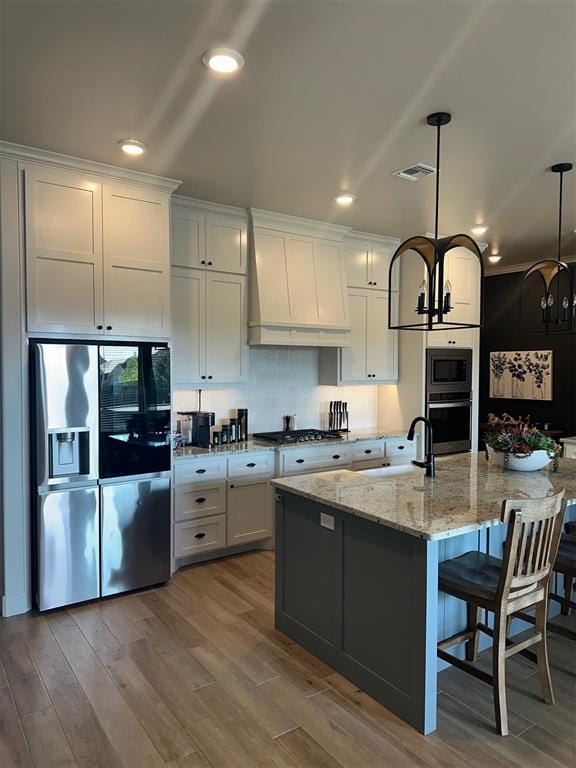 kitchen featuring white cabinetry, hanging light fixtures, stainless steel appliances, a notable chandelier, and an island with sink