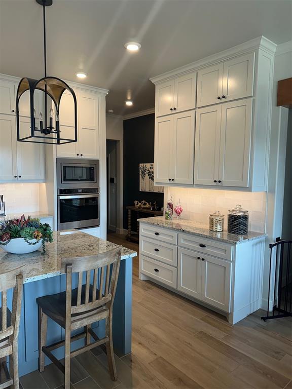 kitchen with white cabinetry, light hardwood / wood-style floors, decorative light fixtures, decorative backsplash, and appliances with stainless steel finishes