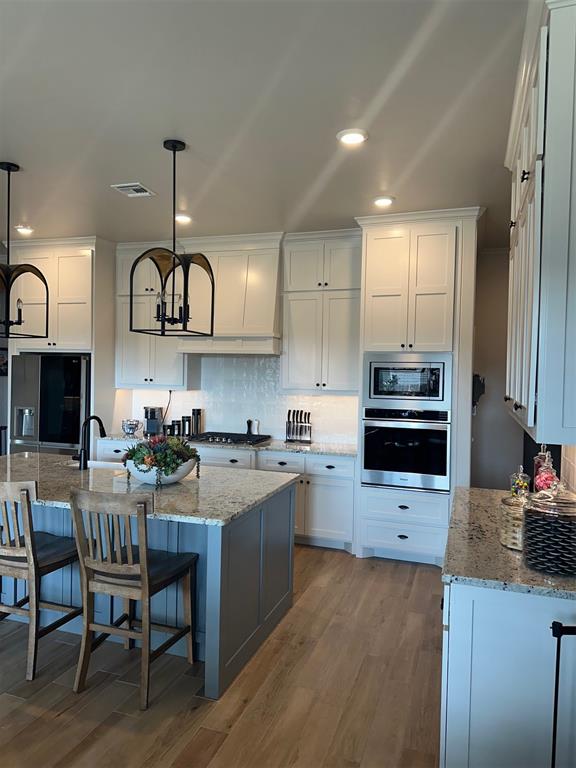 kitchen with light stone counters, stainless steel appliances, white cabinets, hanging light fixtures, and an island with sink