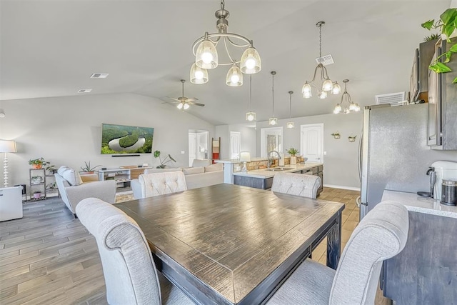 dining room with ceiling fan with notable chandelier, light hardwood / wood-style floors, lofted ceiling, and sink