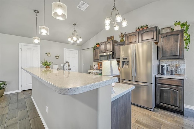 kitchen featuring dark brown cabinetry, a notable chandelier, lofted ceiling, a kitchen island with sink, and appliances with stainless steel finishes