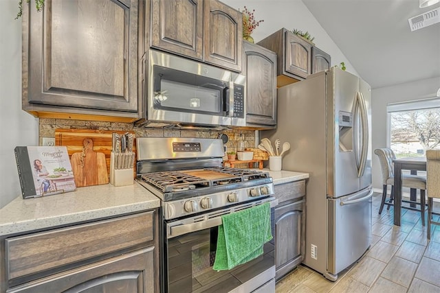 kitchen with light stone countertops, lofted ceiling, appliances with stainless steel finishes, and light hardwood / wood-style flooring