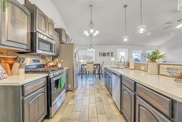 kitchen with sink, hanging light fixtures, stainless steel appliances, vaulted ceiling, and ceiling fan with notable chandelier