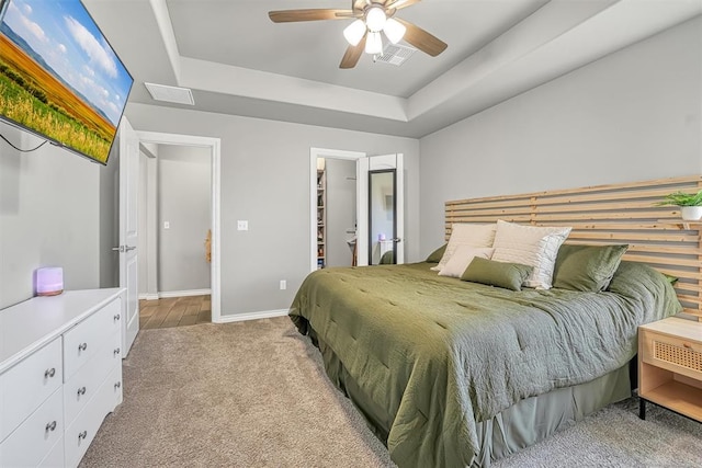 bedroom with light carpet, a raised ceiling, ceiling fan, a spacious closet, and a closet