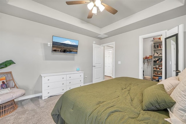 bedroom featuring a raised ceiling, a walk in closet, ceiling fan, light colored carpet, and a closet