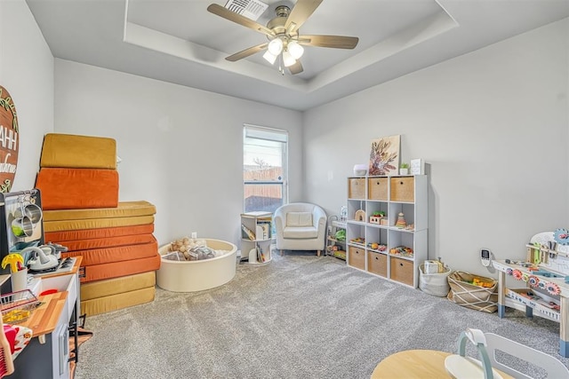 recreation room with carpet floors, a tray ceiling, and ceiling fan