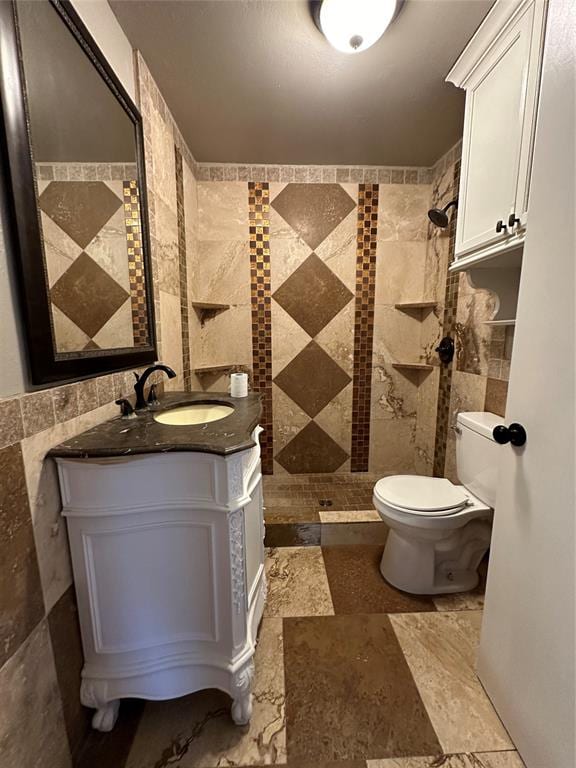 bathroom with vanity, toilet, tiled shower, and tile walls