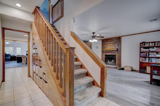 staircase featuring a fireplace, hardwood / wood-style floors, ceiling fan, and ornamental molding