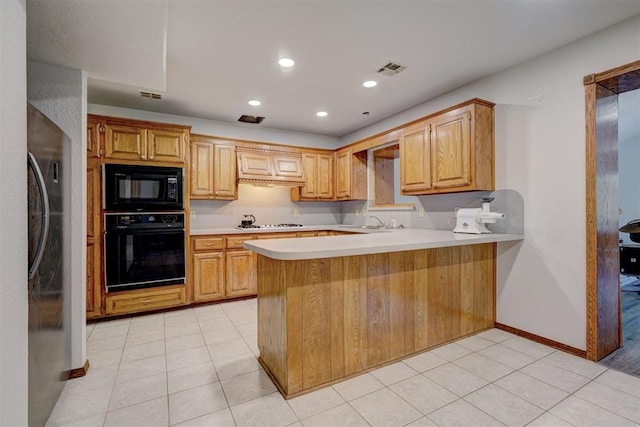 kitchen with sink, kitchen peninsula, light brown cabinetry, light tile patterned floors, and black appliances