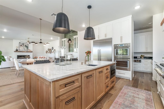 kitchen with a large island with sink, white cabinetry, sink, and pendant lighting