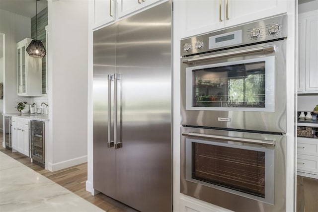 kitchen with appliances with stainless steel finishes, white cabinetry, light stone counters, and beverage cooler