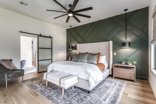 bedroom featuring ceiling fan, a barn door, and light wood-type flooring