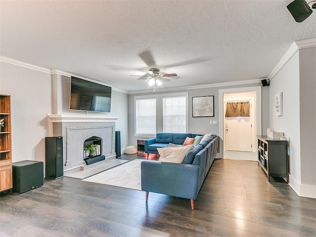 living room with ceiling fan, dark hardwood / wood-style floors, crown molding, a textured ceiling, and a fireplace