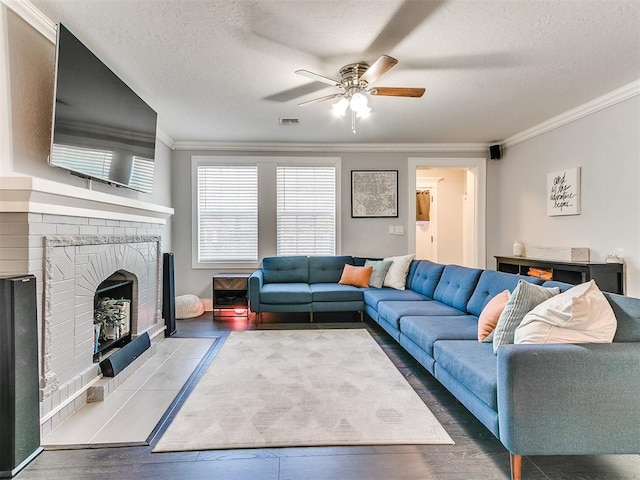 living room featuring ceiling fan, a brick fireplace, hardwood / wood-style floors, a textured ceiling, and ornamental molding