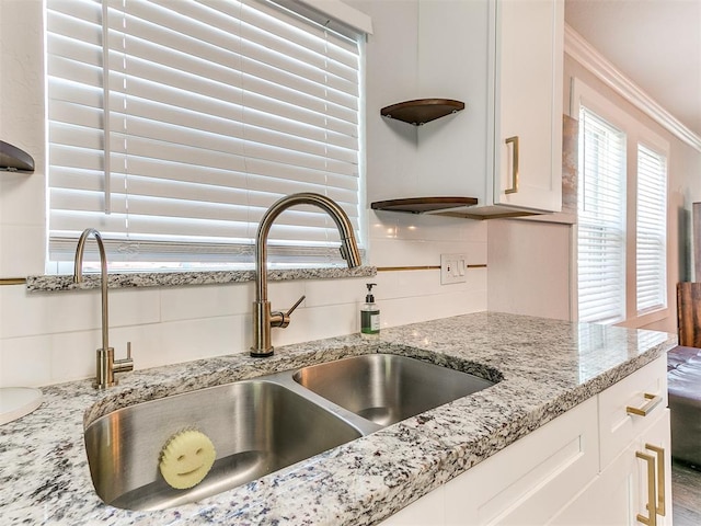 details featuring backsplash, sink, ornamental molding, light stone counters, and white cabinetry