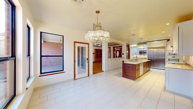 kitchen with appliances with stainless steel finishes, light stone counters, white cabinets, hanging light fixtures, and an island with sink