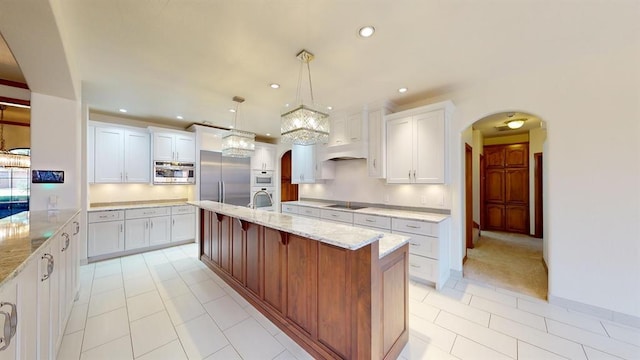 kitchen featuring white cabinetry, light stone counters, built in appliances, decorative light fixtures, and a kitchen island with sink