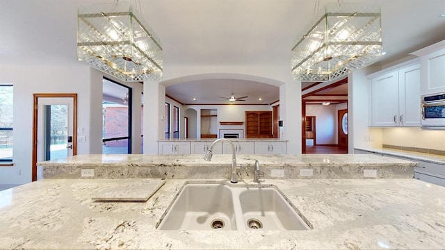 kitchen with pendant lighting, white cabinets, sink, ceiling fan, and light stone counters