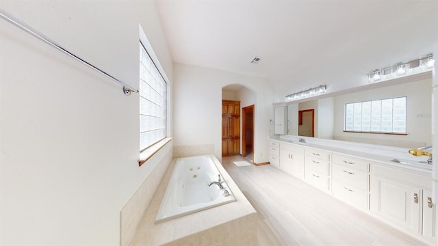 bathroom with vanity, a relaxing tiled tub, and a wealth of natural light