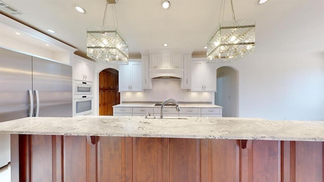 kitchen featuring white cabinetry, sink, premium range hood, decorative light fixtures, and stainless steel built in fridge