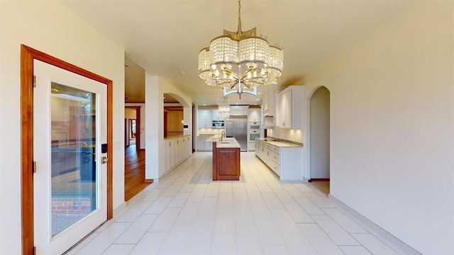 kitchen with pendant lighting, stainless steel built in refrigerator, a center island with sink, a notable chandelier, and white cabinetry