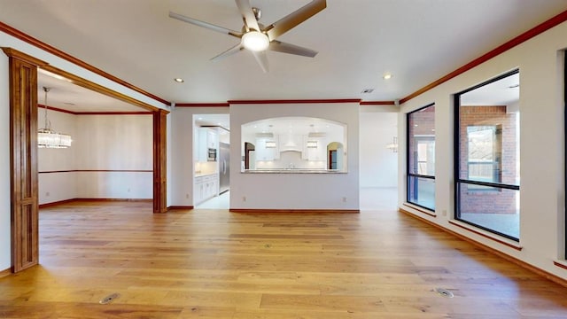 unfurnished living room featuring ceiling fan with notable chandelier, light wood-type flooring, and ornamental molding