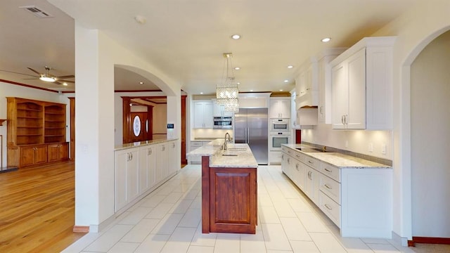 kitchen featuring white cabinets, built in fridge, an island with sink, and hanging light fixtures