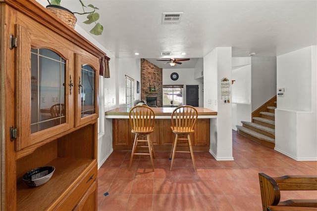 kitchen featuring kitchen peninsula, a kitchen breakfast bar, a fireplace, ceiling fan, and tile patterned flooring