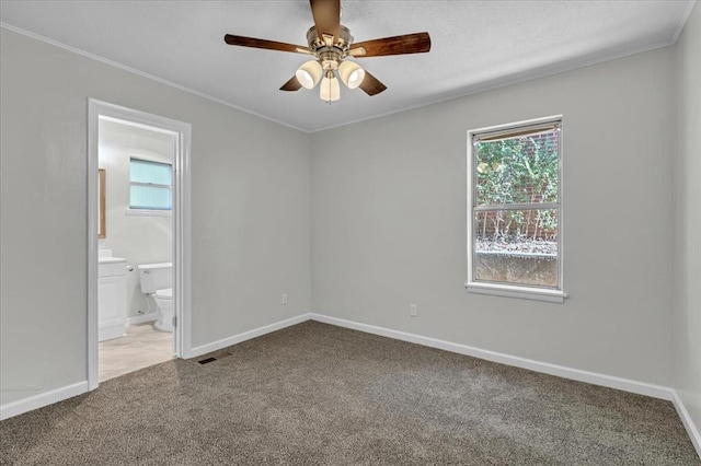 unfurnished bedroom with carpet flooring, ceiling fan, ensuite bath, and multiple windows