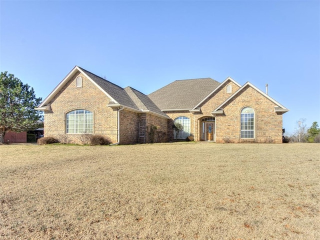 view of front of property featuring a front yard, brick siding, and roof with shingles