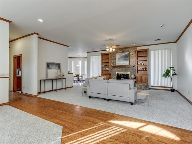 living area with a brick fireplace, crown molding, baseboards, wood finished floors, and a ceiling fan