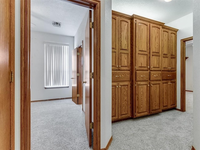 hall featuring a textured ceiling, baseboards, visible vents, and light carpet