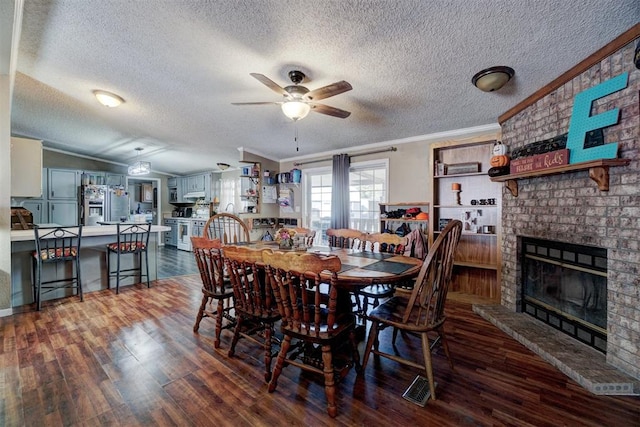 dining room with a ceiling fan, wood finished floors, visible vents, crown molding, and a brick fireplace