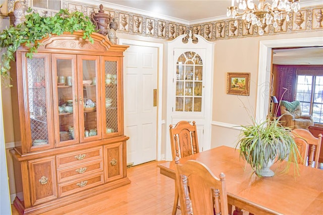 dining space with light wood-type flooring, crown molding, and a notable chandelier